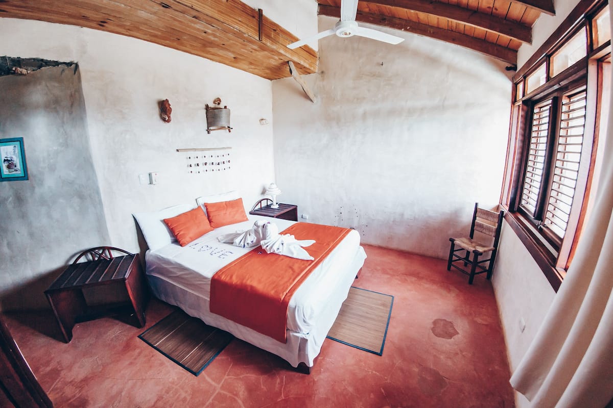 A room with a bed, a chair, a small table, and a window with bars.