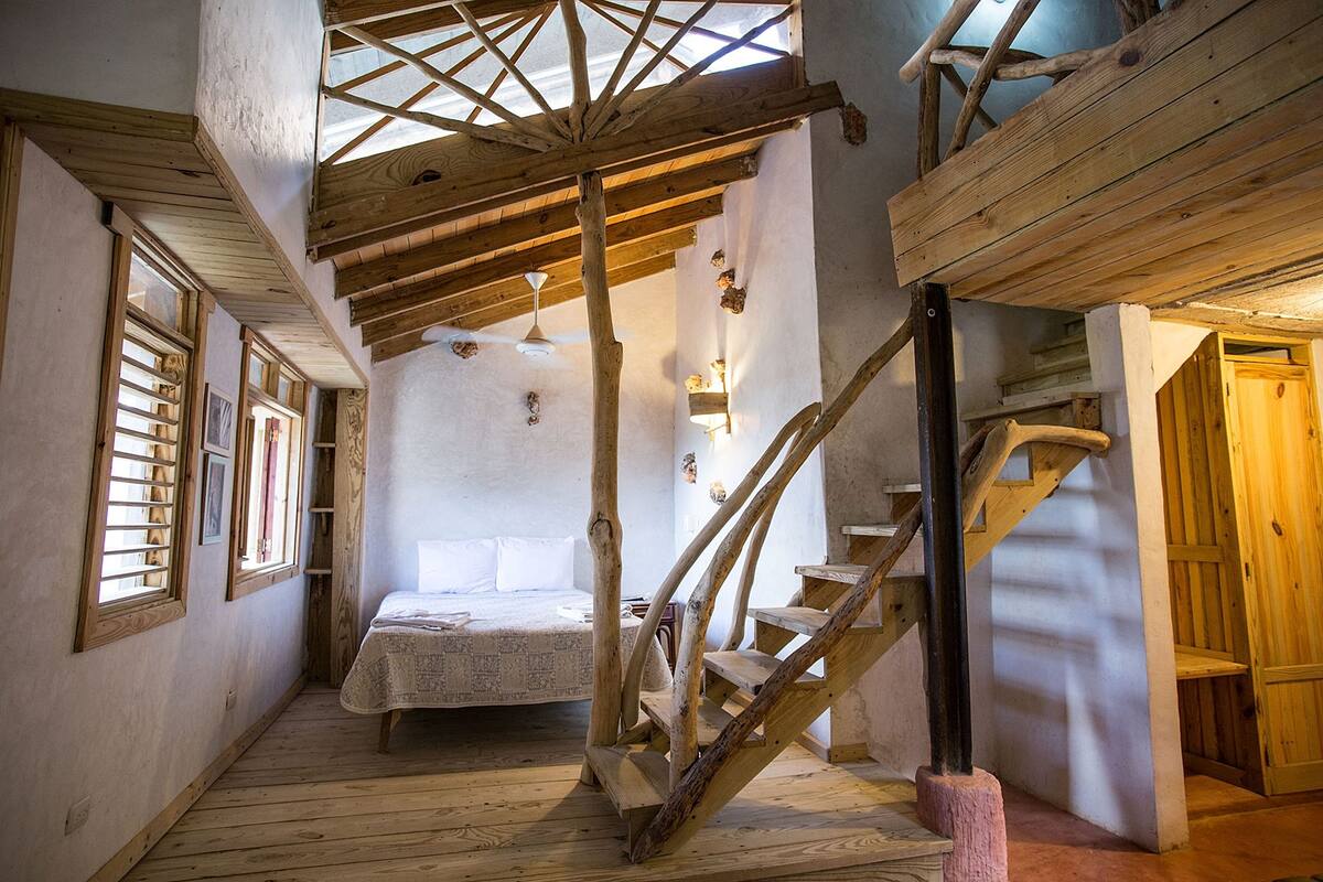 A rustic room with a wooden staircase, a bed with a white bedspread, and a skylight.
