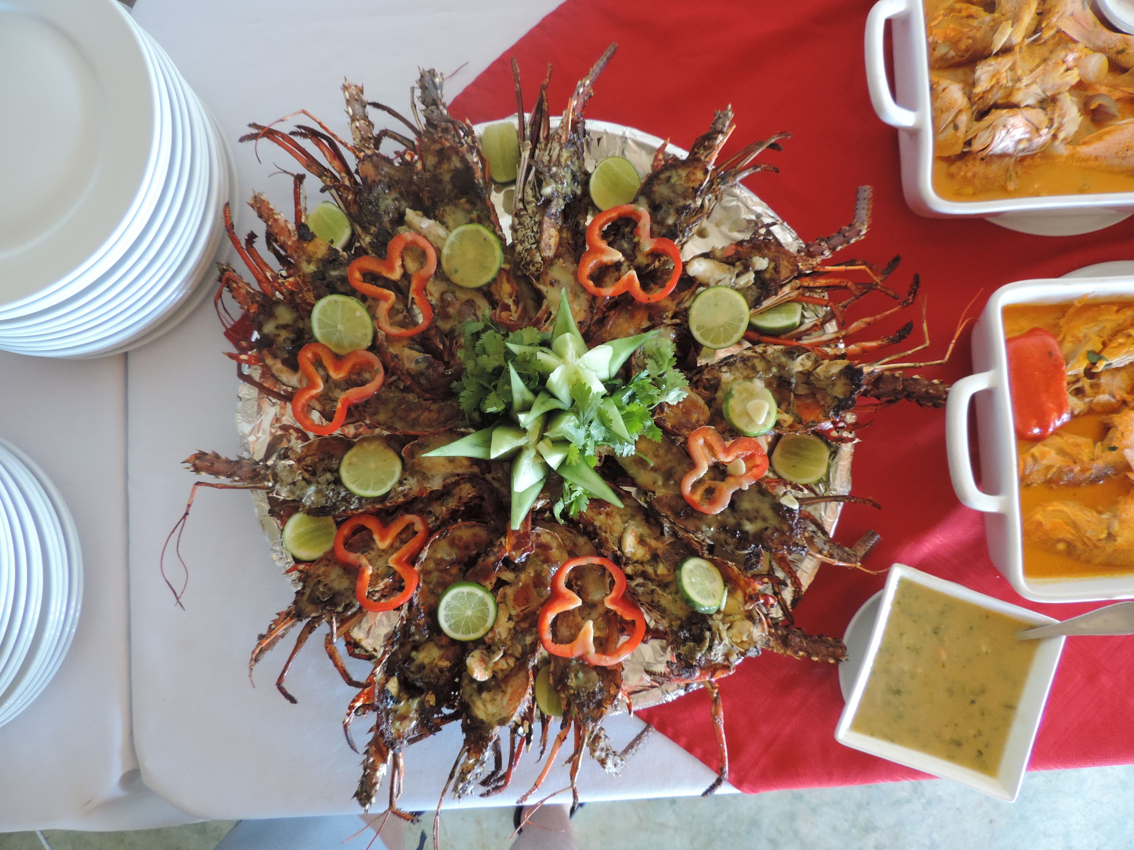 A seafood platter with various garnishes on a white plate, accompanied by bowls of soup and other dishes on a red tablecloth.