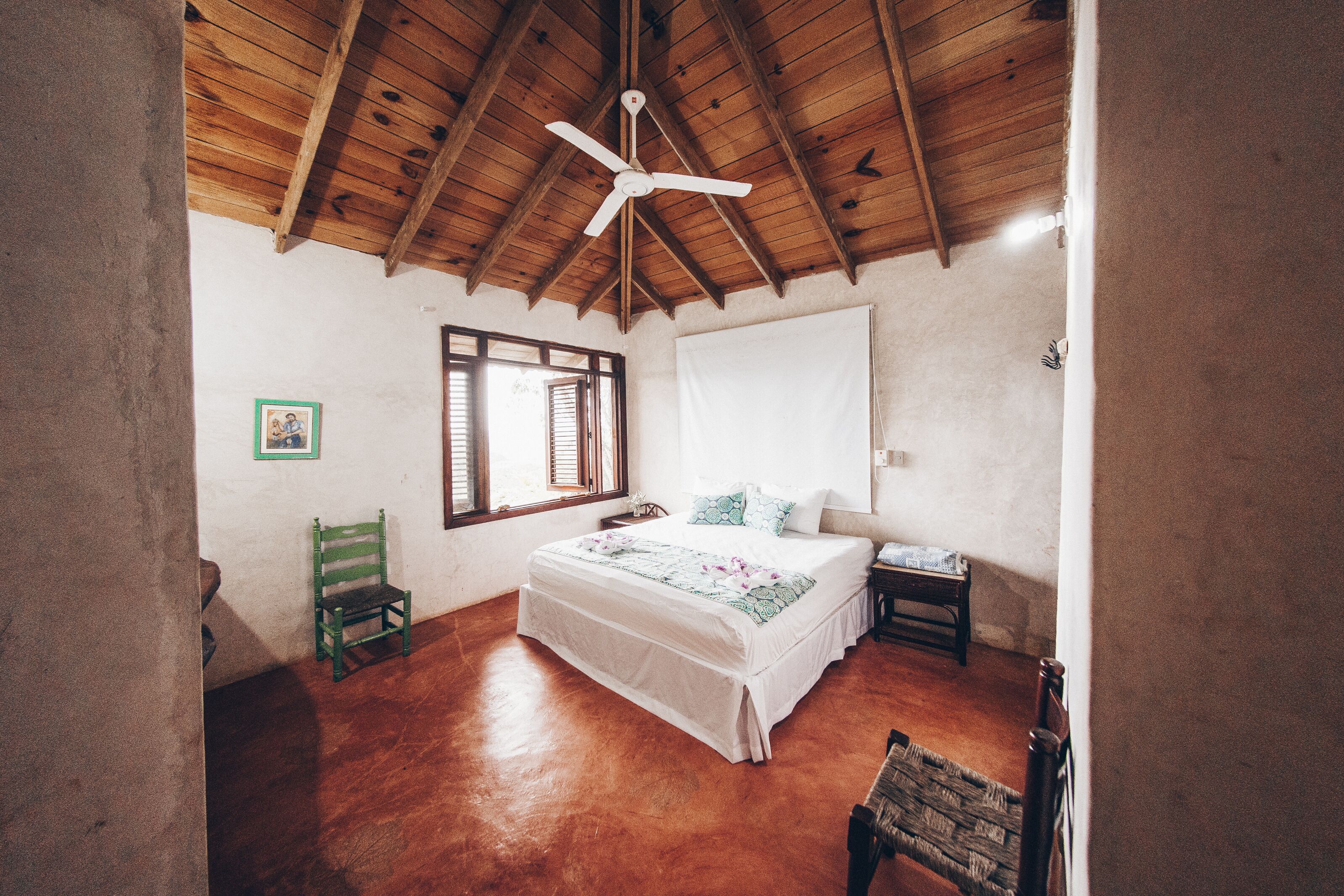 Ein Schlafzimmer mit Holzbalkendecke, einem Bett mit weißer Bettdecke, einem grünen Sessel und einem Nachttisch.
