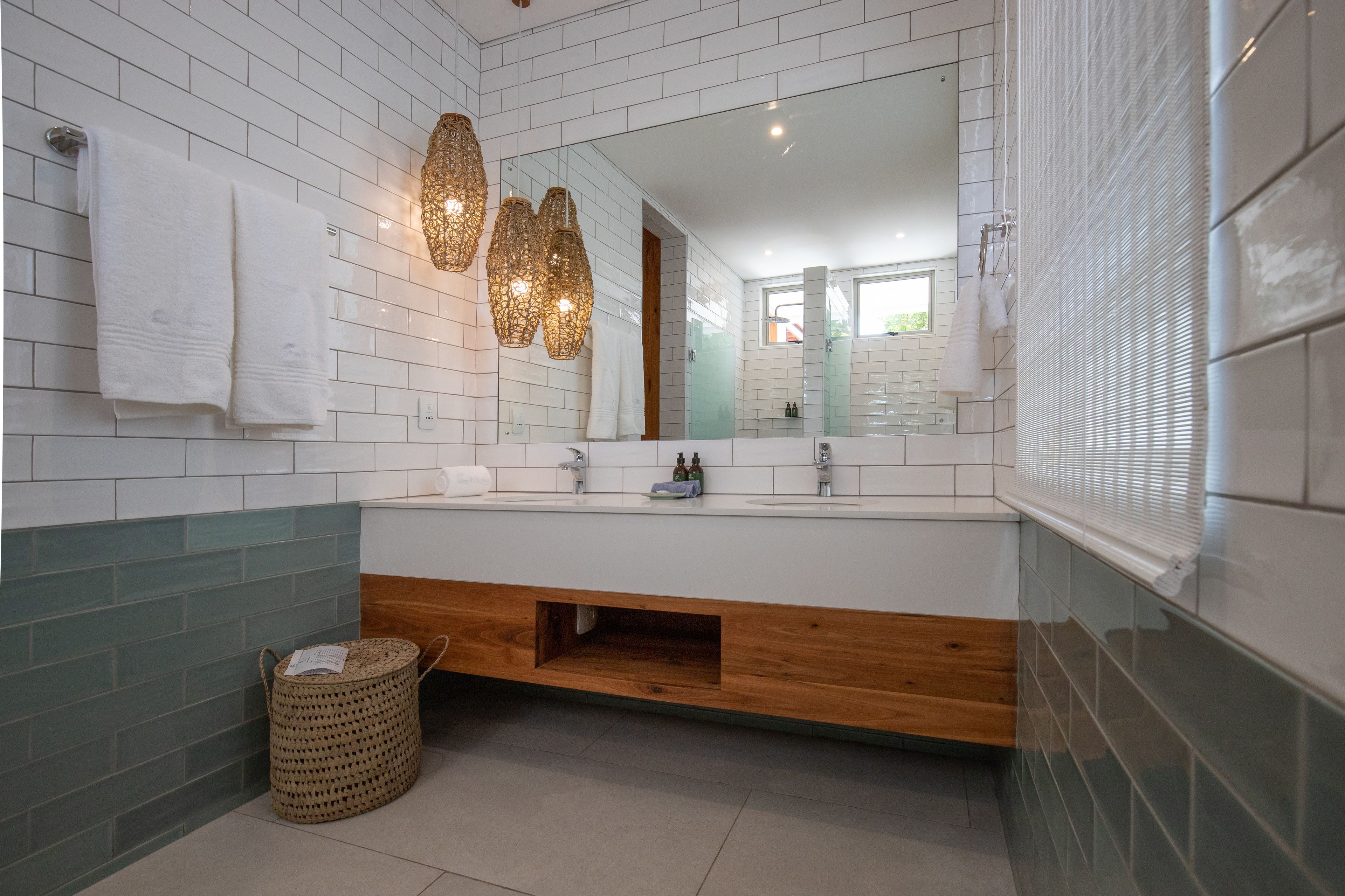 Un baño moderno con paredes de azulejos blancos, un tocador de madera y un espejo grande.