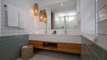 Un baño moderno con paredes de azulejos blancos, un tocador de madera y un espejo grande.
