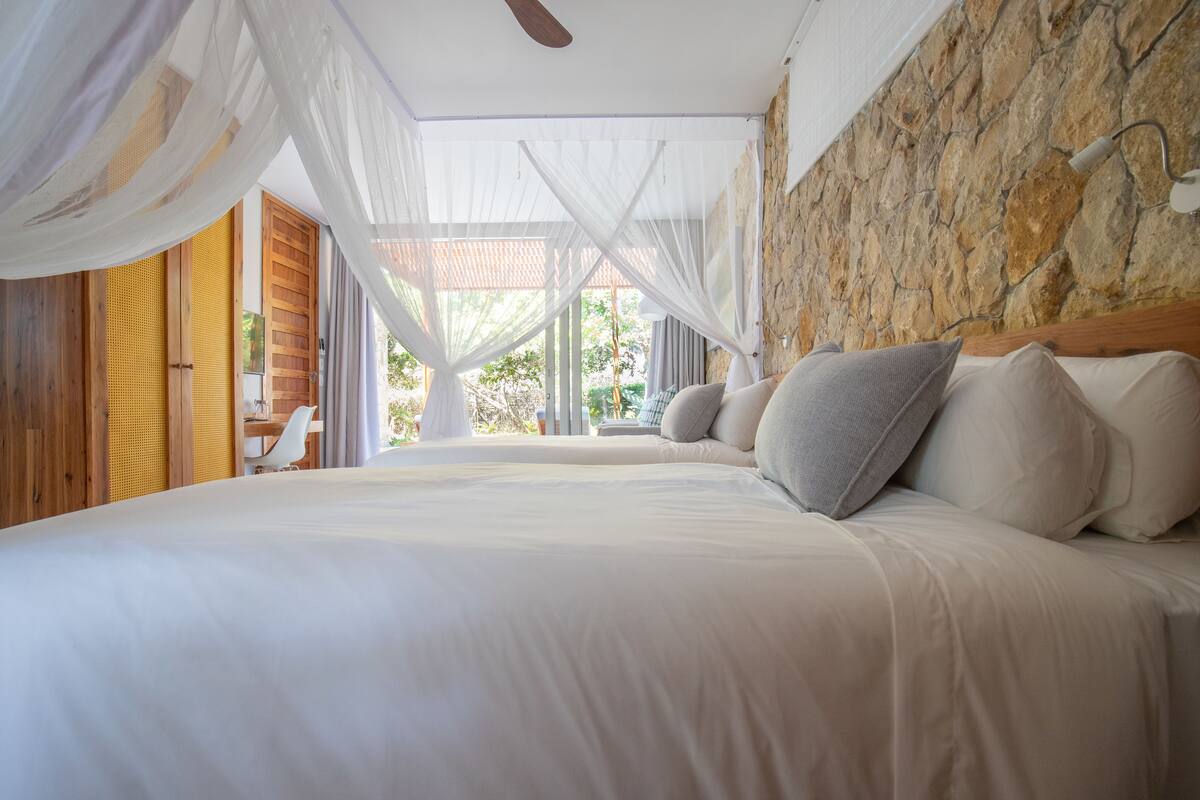 Un dormitorio con una cama grande, cortinas blancas, un cabecero de madera y una pared de piedra.