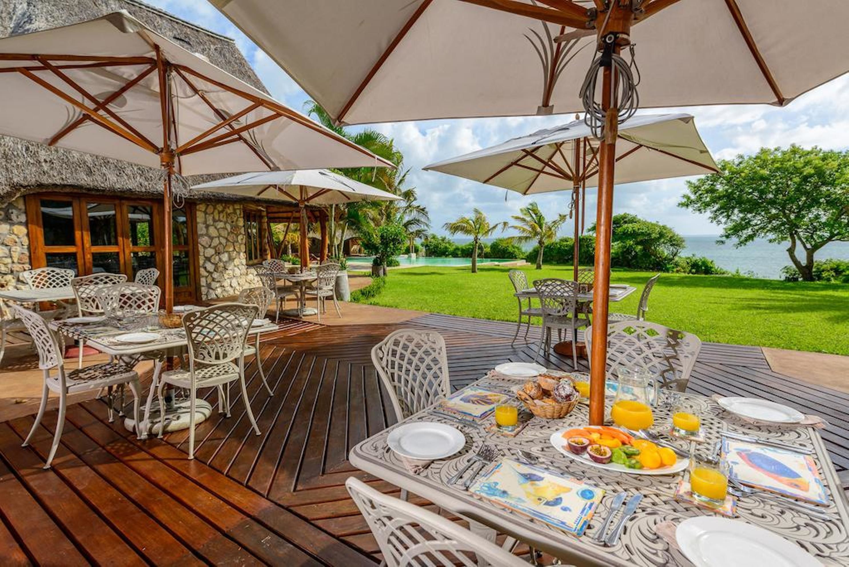An outdoor dining area with tables and chairs, umbrellas, and a view of the sea.
