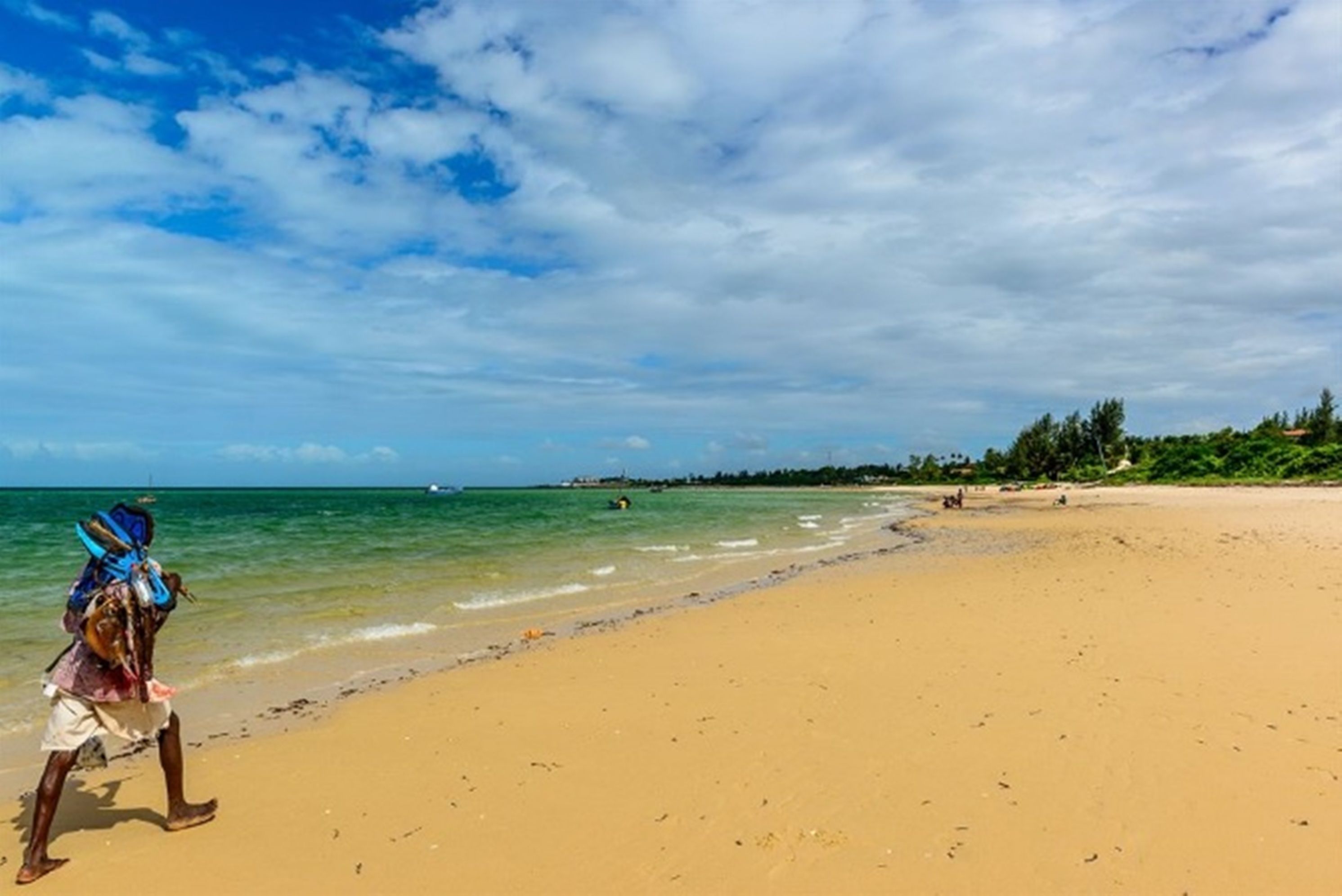 A wide sandy beach with clear blue water and a partly cloudy sky.