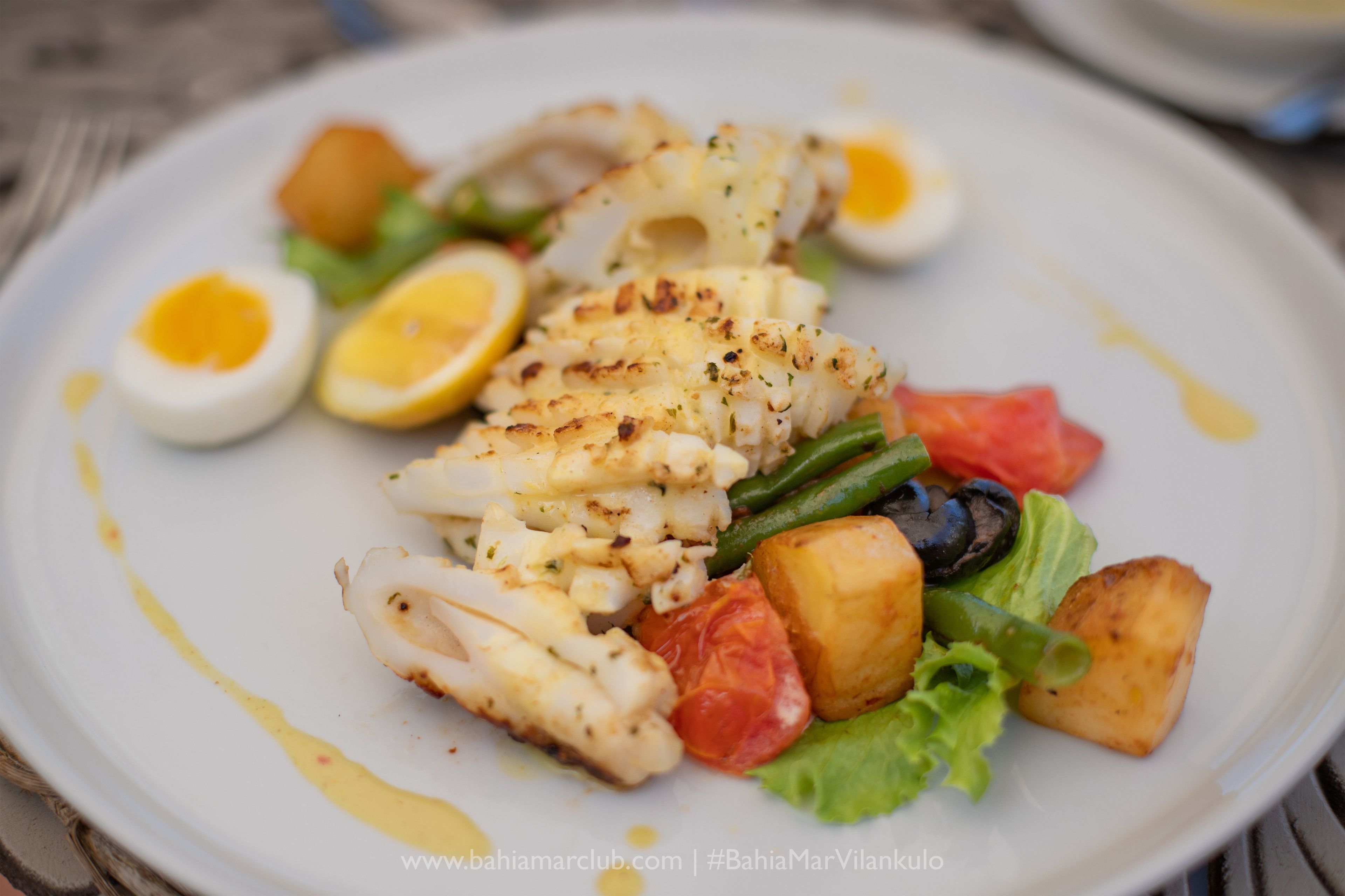A plate of grilled fish, lemon slices, and vegetables.