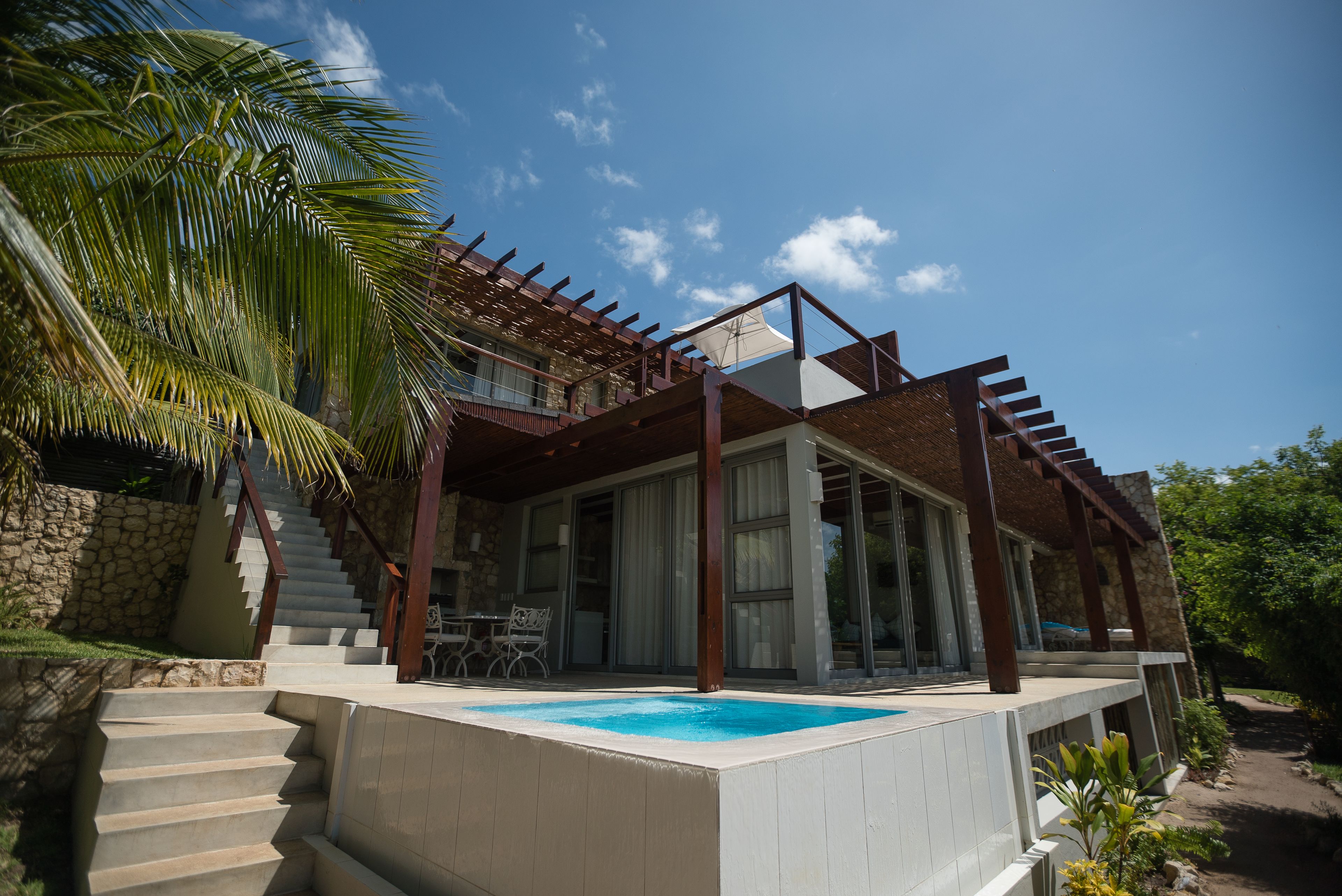 A modern house with a swimming pool, a stone wall, and a staircase leading to a balcony.