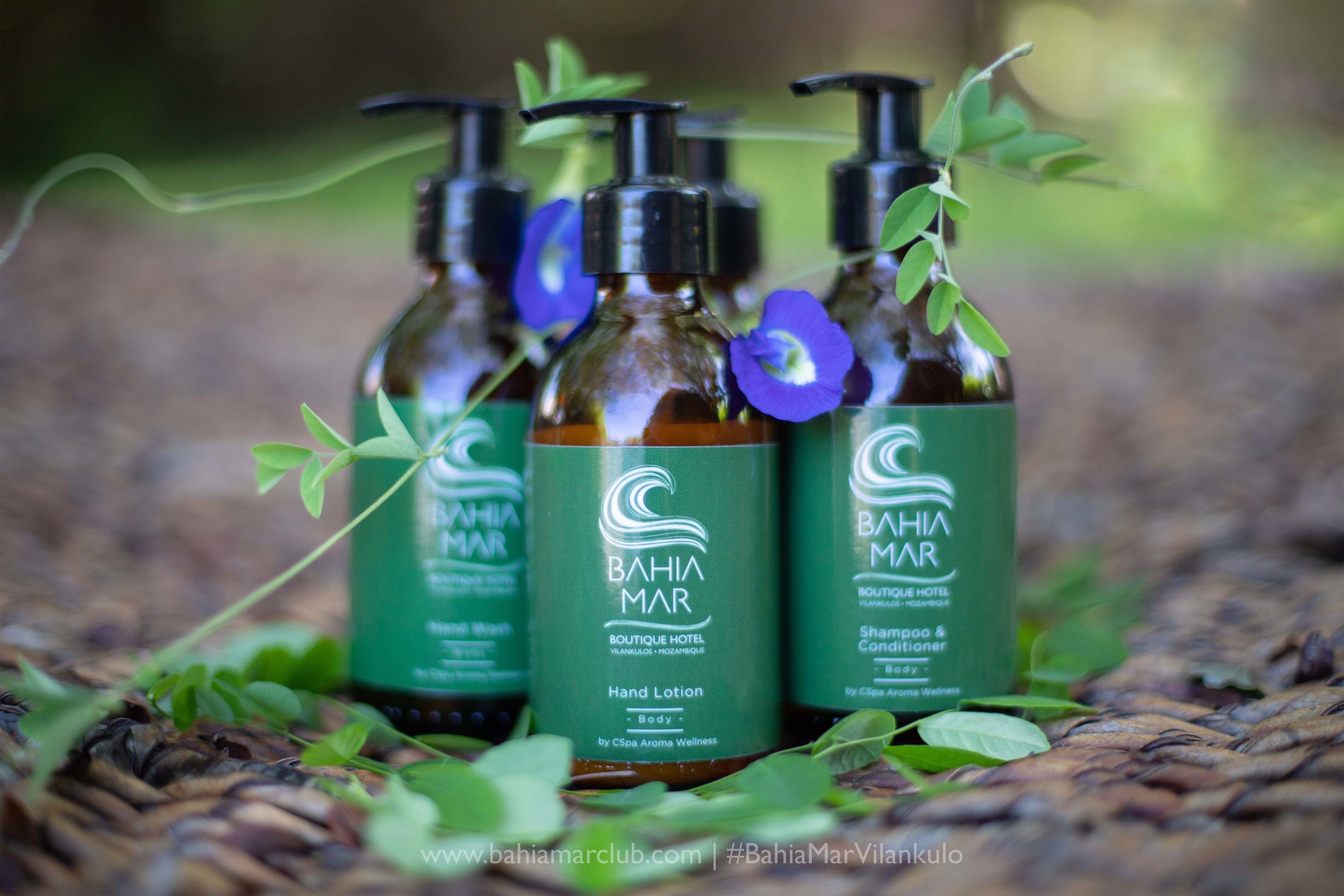 Three bottles of Bahia Mar hand lotion and shampoo & conditioner on a woven surface.