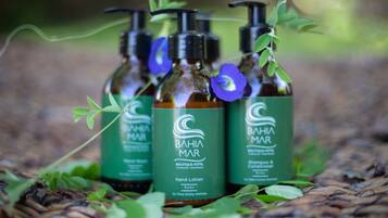 Three bottles of Bahia Mar hand lotion and shampoo & conditioner on a woven surface.