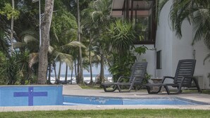 Zona de piscina con sillones de descanso, palmeras y vistas al océano.