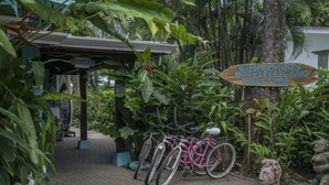 Un área de recepción con un letrero de madera que da la bienvenida a los huéspedes, bicicletas y exuberante vegetación.