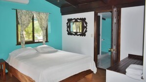Un dormitorio con cama, ventana con cortinas, espejo y puerta que da a otra habitación.