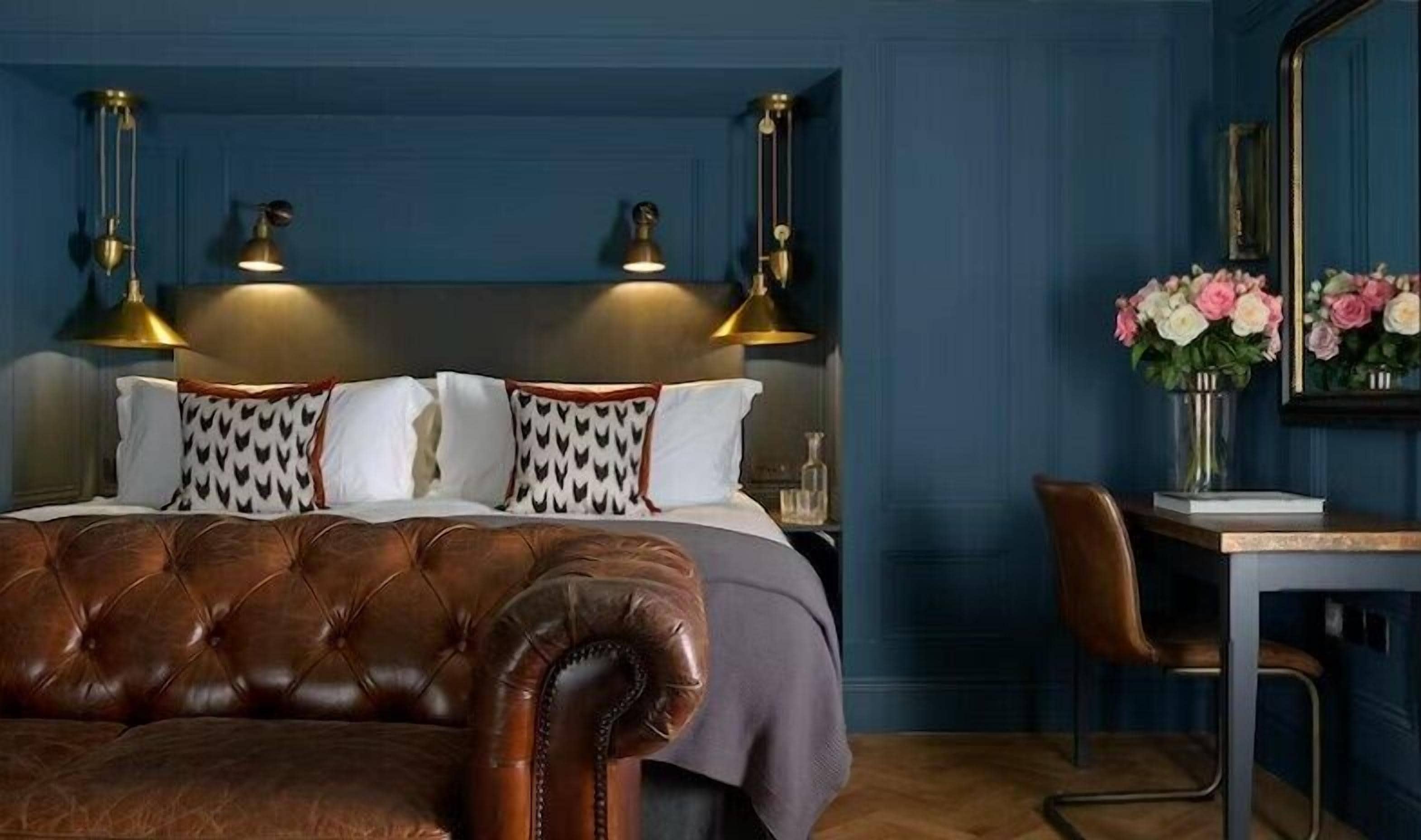 A bedroom with a tufted leather headboard, a wooden desk, and a mirror.