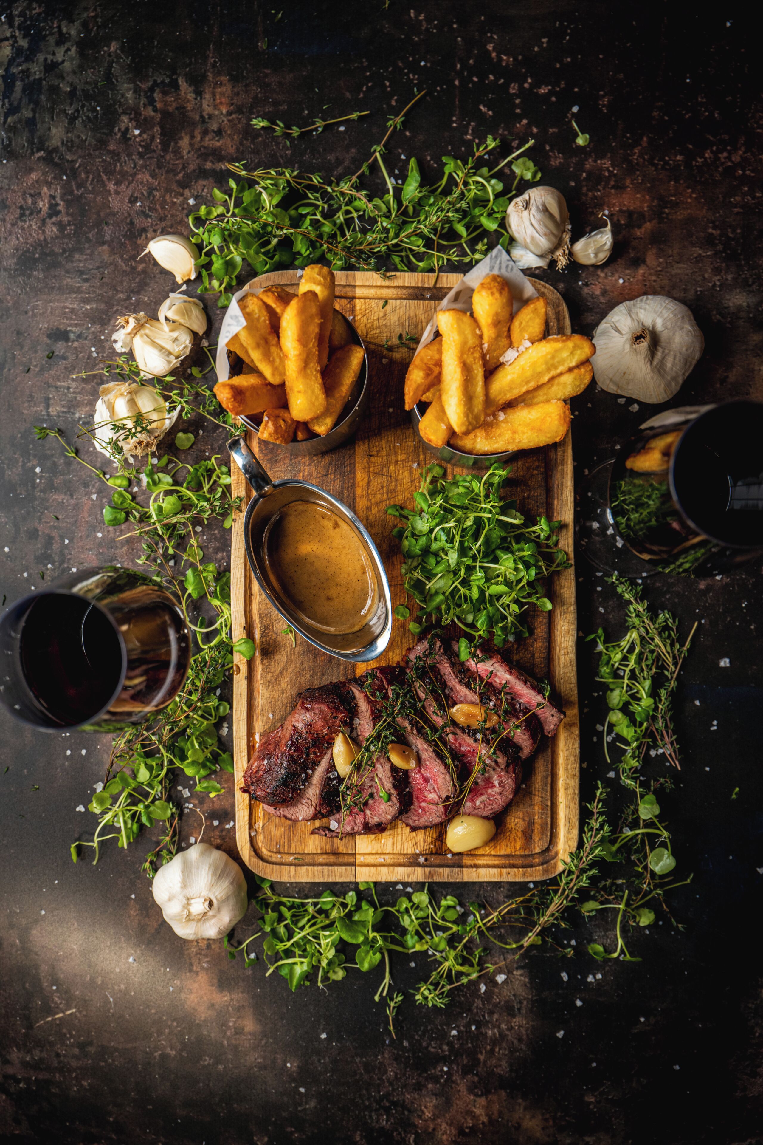 Uma tábua de madeira com bife, batatas fritas e uma tigela de molho gravy.