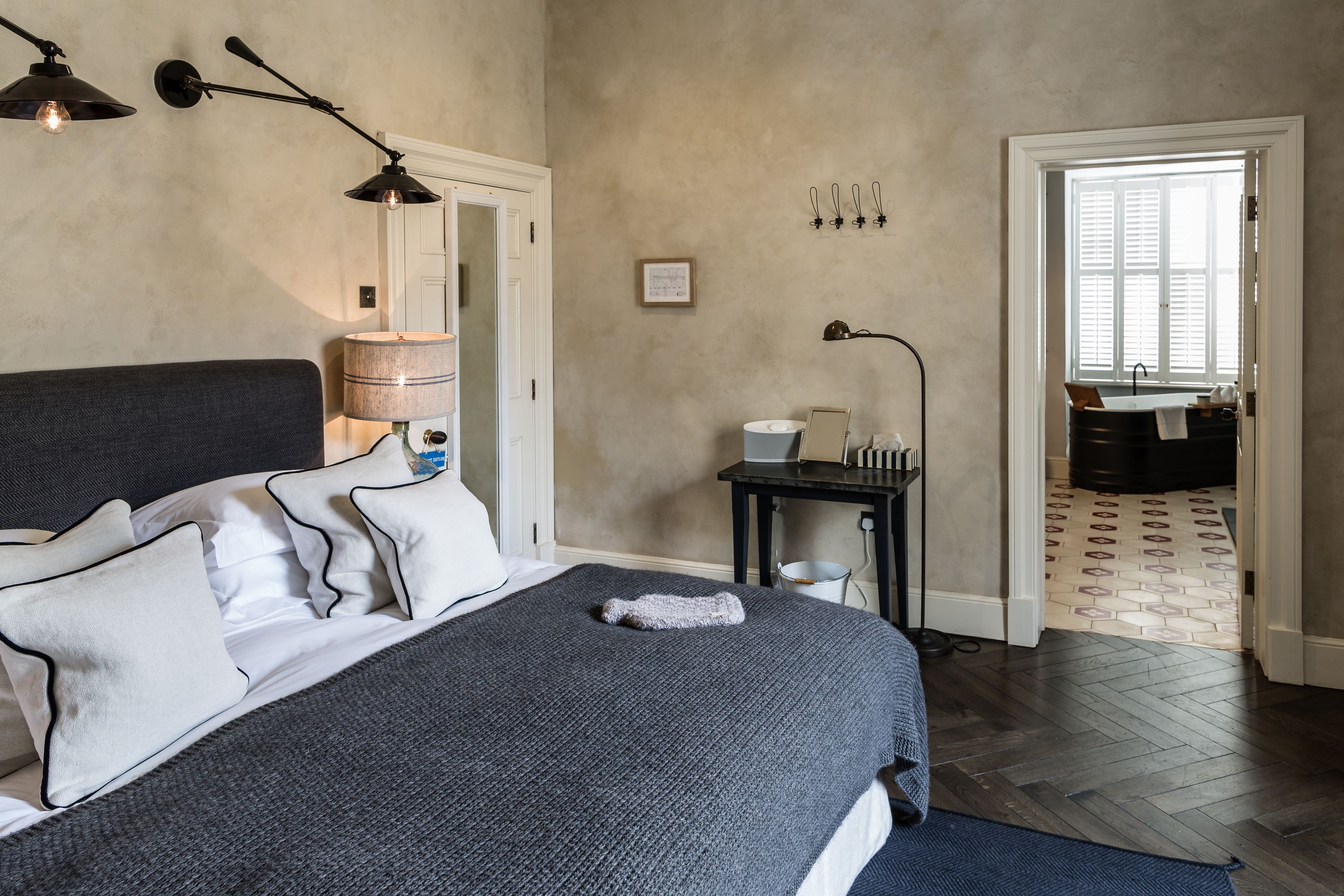 A bedroom with a bed, bedside table, lamp, and a view of the bathroom through an open door.