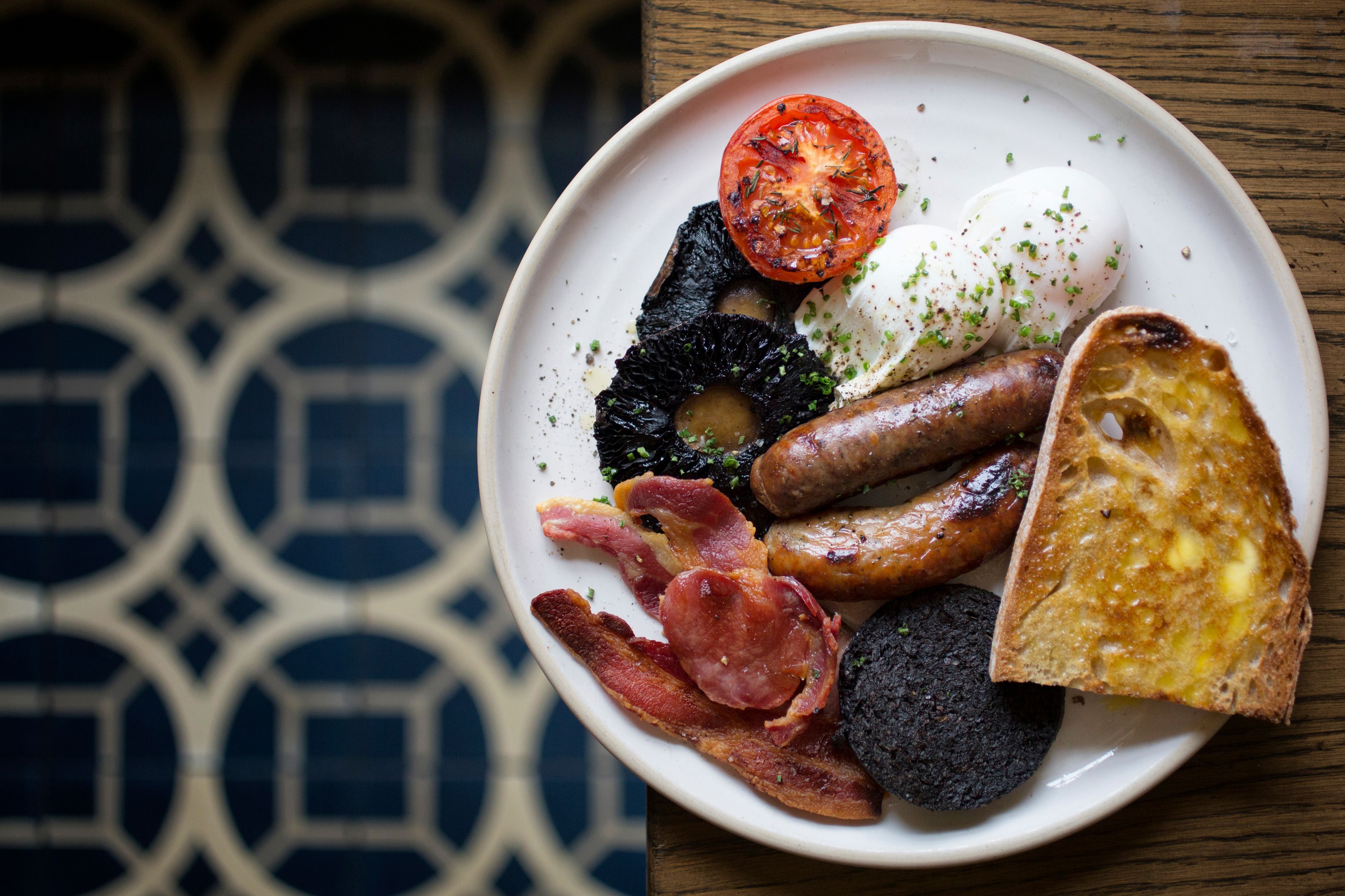 A plate of breakfast food including sausages, bacon, eggs, toast, and a tomato.