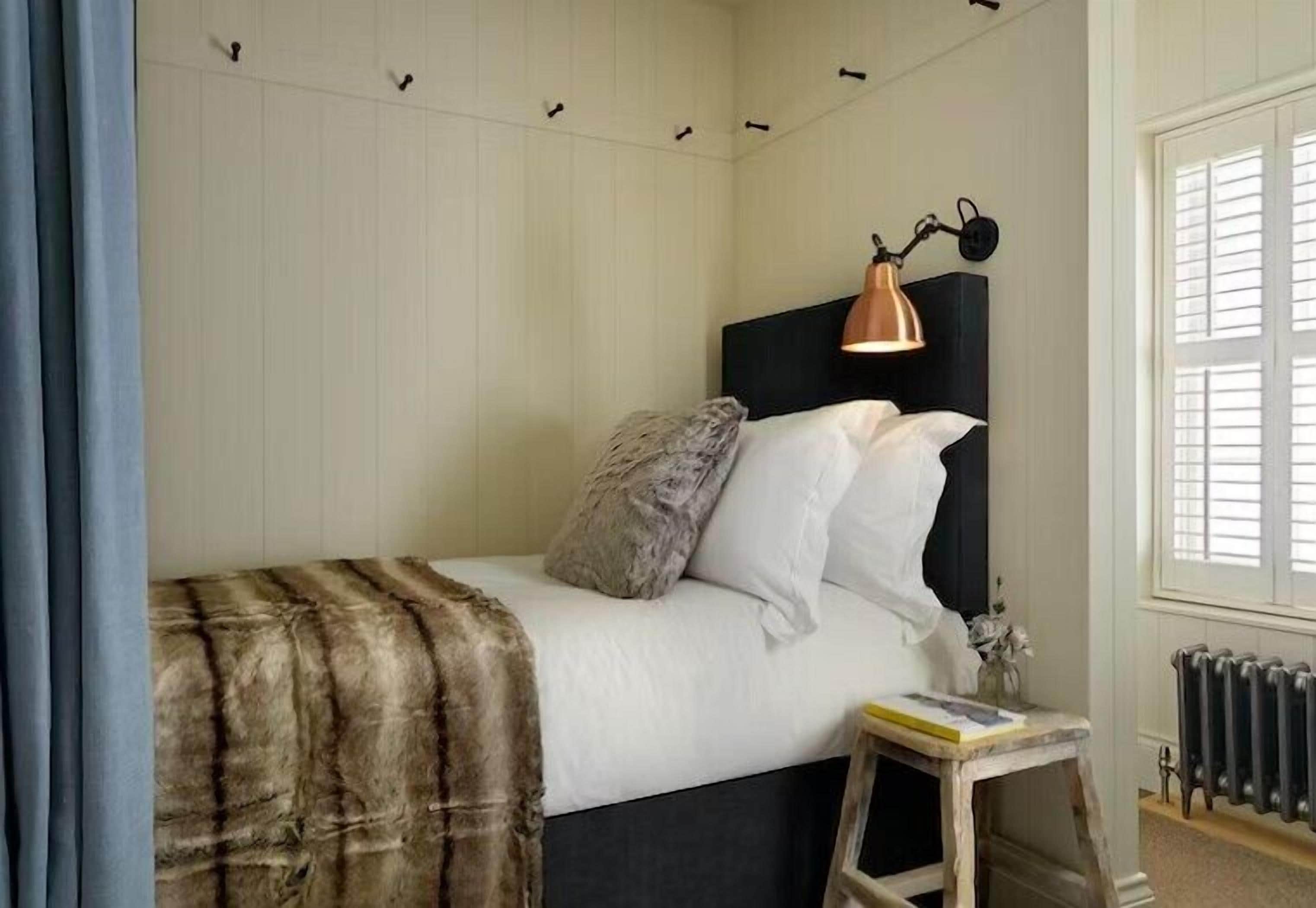 A bedroom with a bed, a headboard, a lamp, a radiator, and a window.