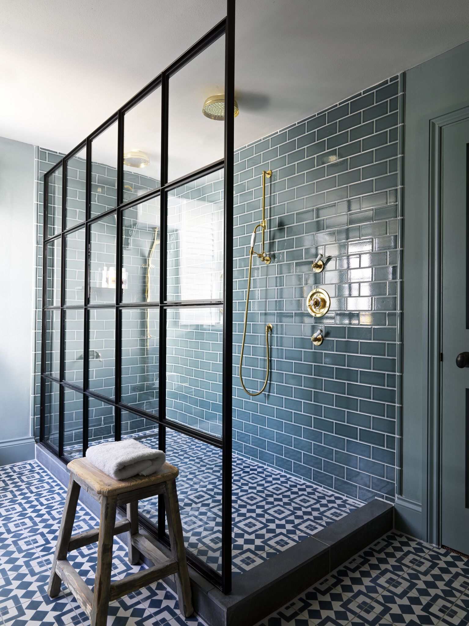 A bathroom with a glass partition, a shower with a gold showerhead, and a patterned floor.