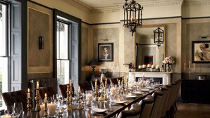Een formele eetzaal met een lange tafel gedekt voor een maaltijd, elegante stoelen en een kroonluchter.