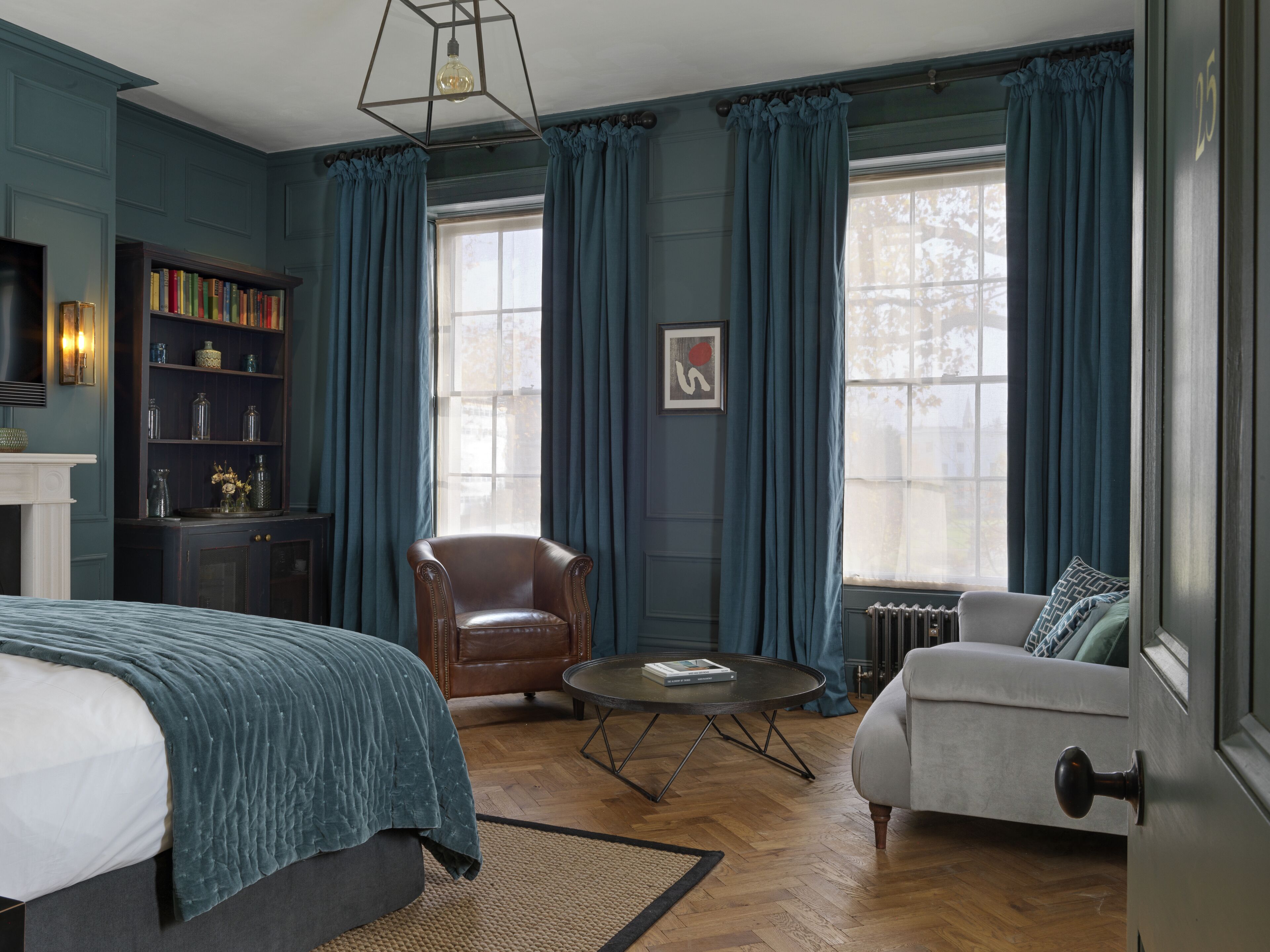 A room with a bed, a leather armchair, a sofa, a small round table, a bookshelf, and a fireplace.