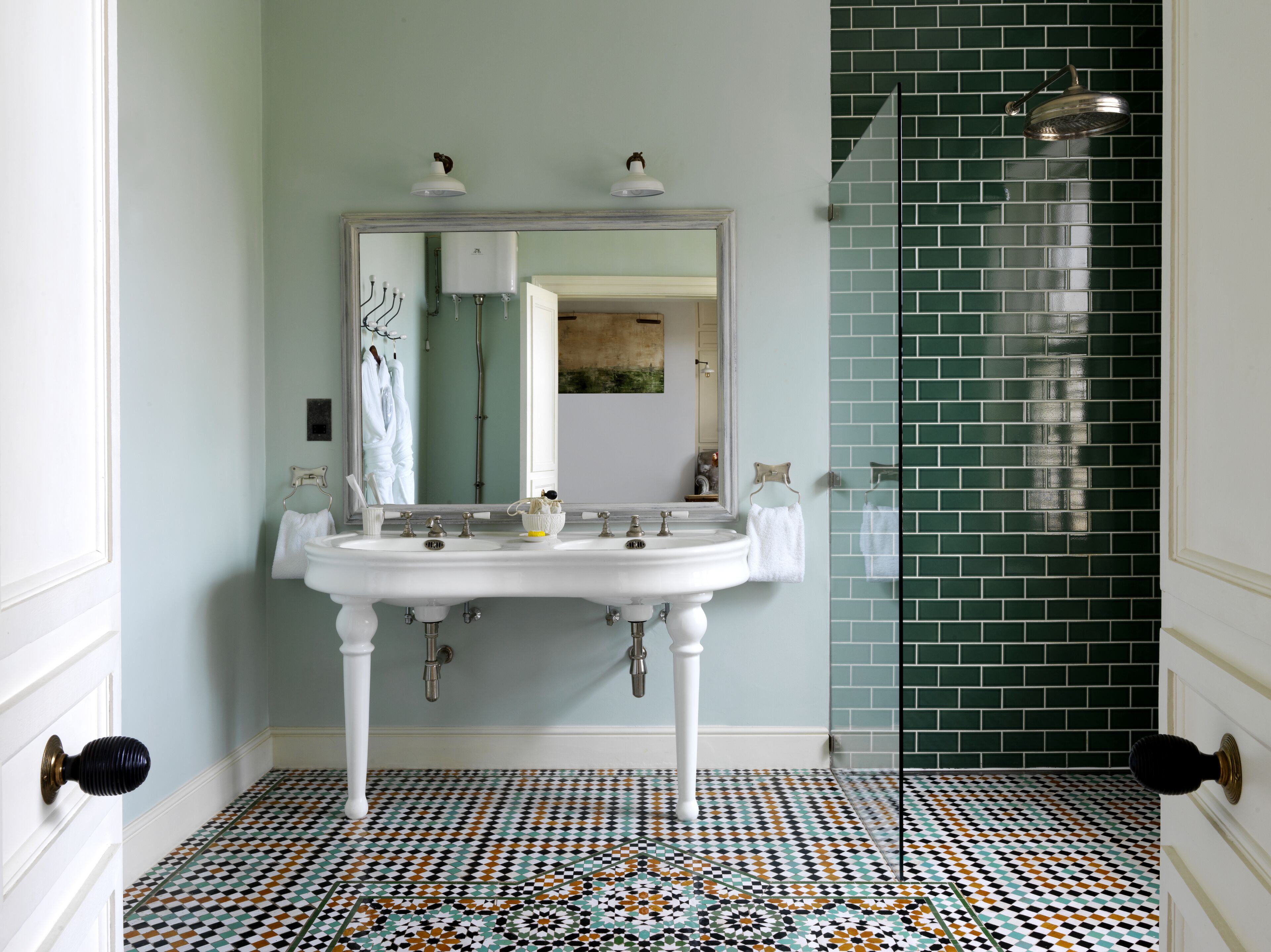 A bathroom with a white sink, two mirrors, a showerhead, and a tiled floor.