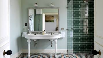 A bathroom with a white sink, two mirrors, a showerhead, and a tiled floor.