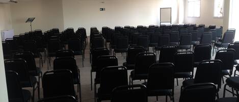 A conference room with rows of black chairs, a whiteboard, and a projector screen.