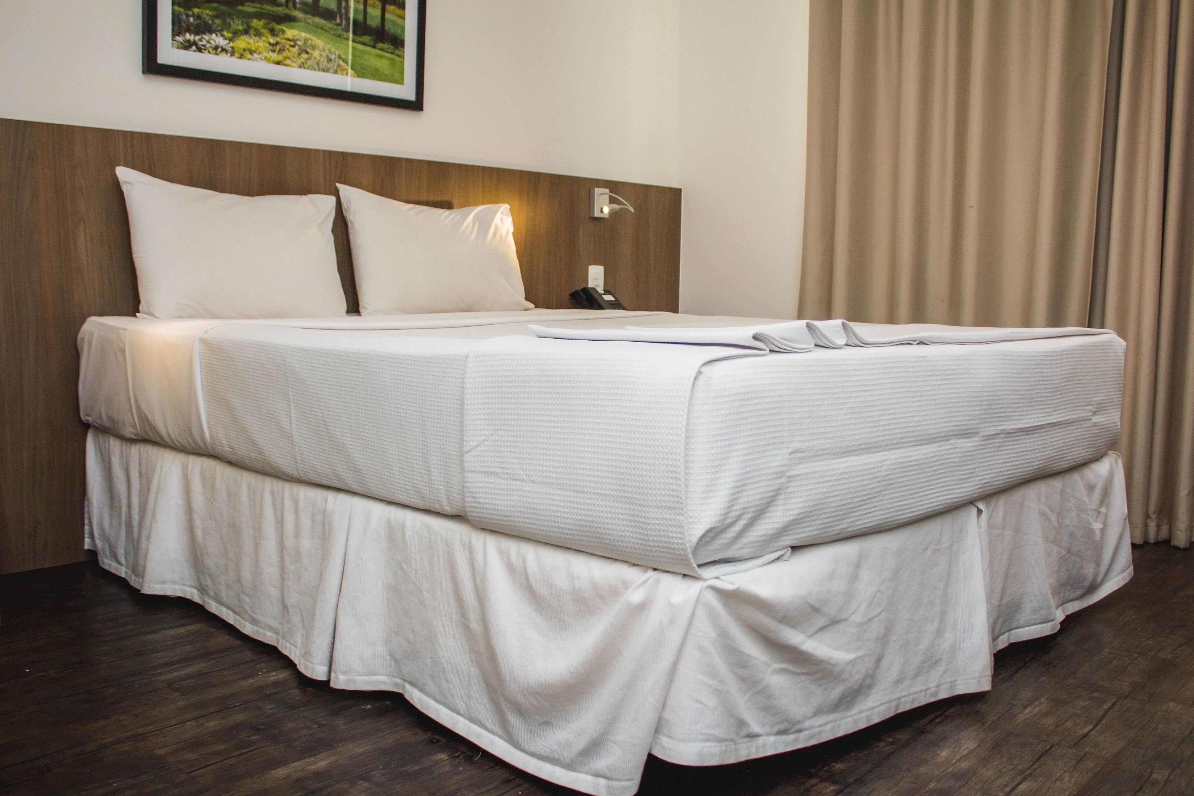 A neatly made double bed with a wooden headboard, a bedside table with a lamp, and a framed picture on the wall.