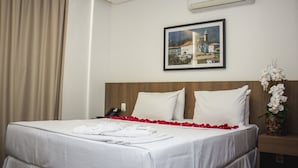 Una habitación de hotel con una cama bien hecha, un cuadro en la pared y un jarrón con flores blancas sobre la mesita de noche.