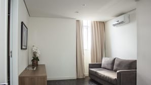 Una sala de estar moderna con un sofá gris, una mesita de madera con un jarrón de flores y un ventanal con cortinas color beige.