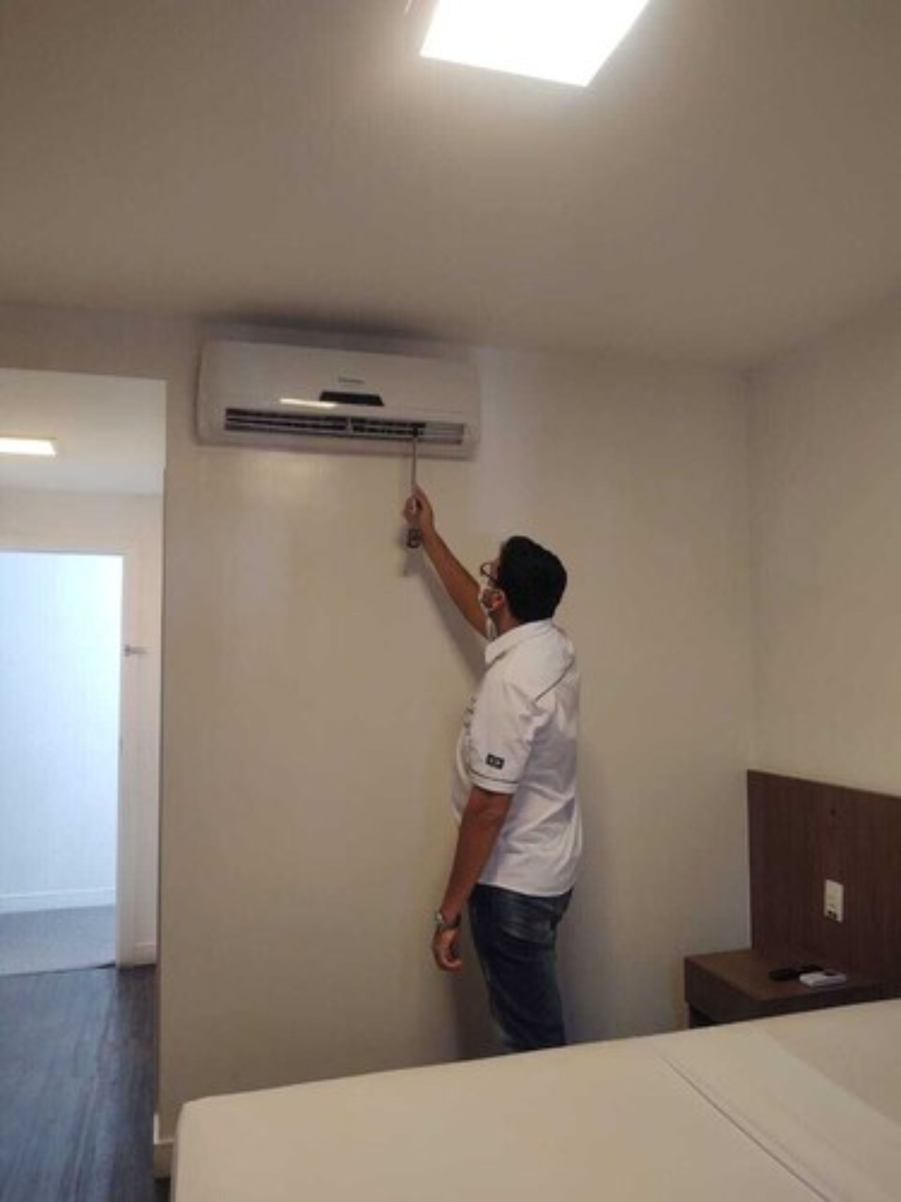 Une personne qui règle un appareil de climatisation fixé au mur dans une chambre d’hôtel.