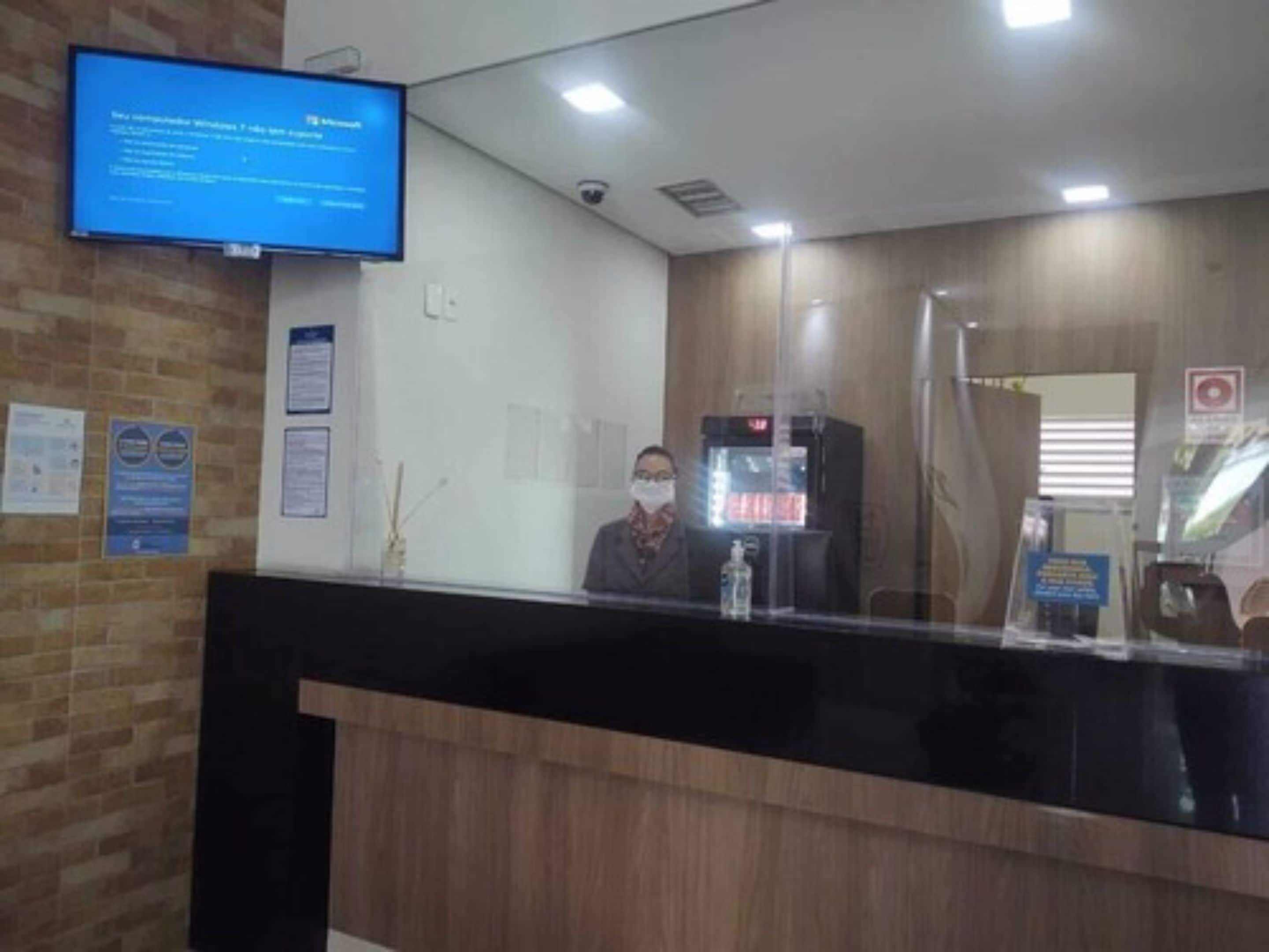 A reception desk with a computer monitor displaying a message, a water dispenser, and a glass partition.