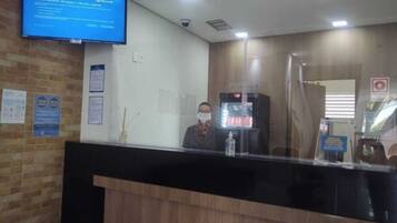Un mostrador de recepción con un monitor que muestra un mensaje, un dispensador de agua y un panel de vidrio.