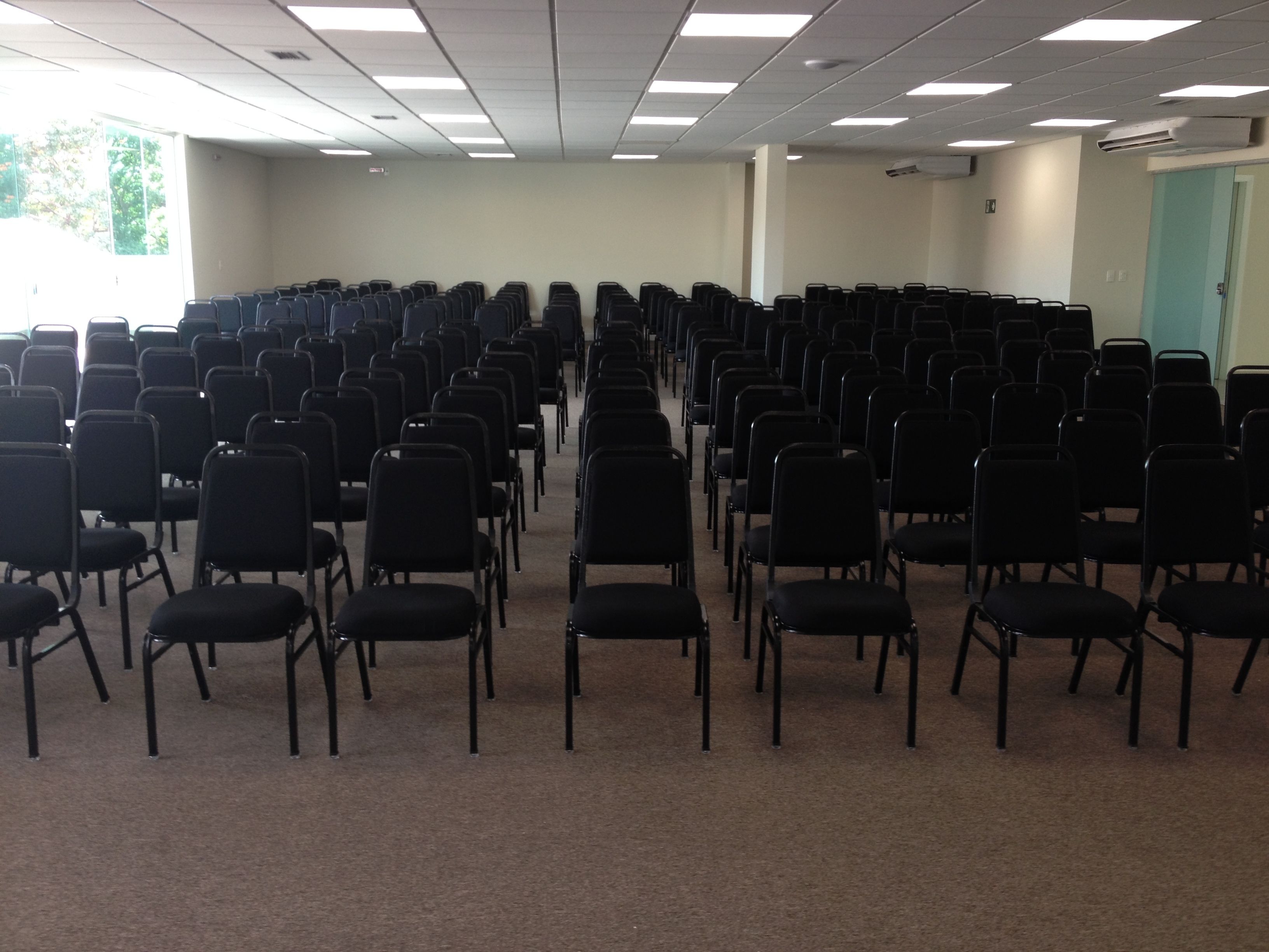 A conference room with rows of black chairs, carpeted floor, and a plain wall with a door.