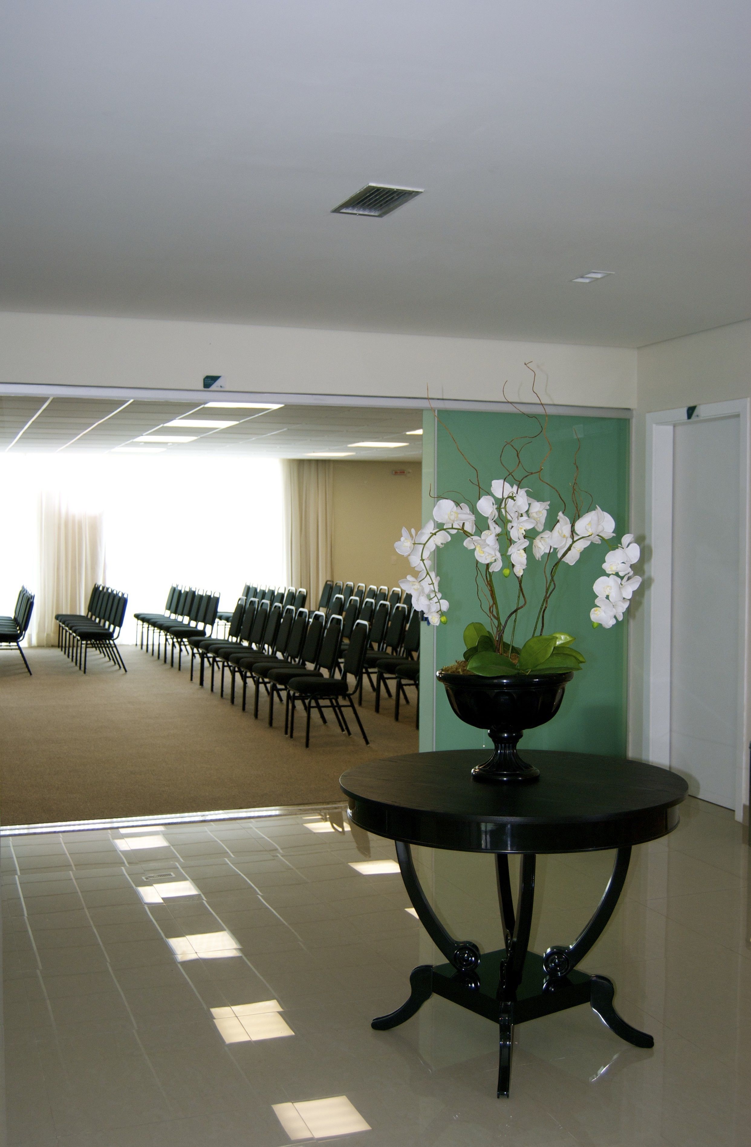 A conference room with rows of chairs, a black table with a flower vase, and a green accent wall.