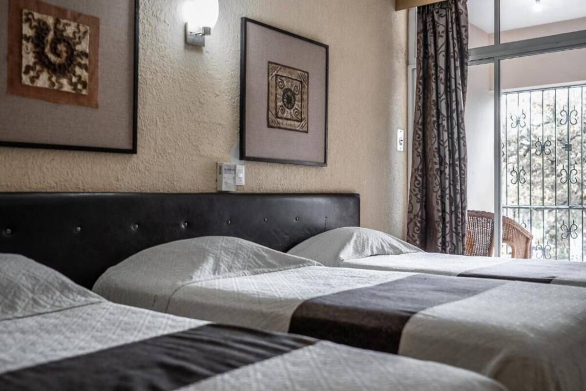 A hotel room with a large bed, two bedside tables, and a view of a balcony with metal railings.