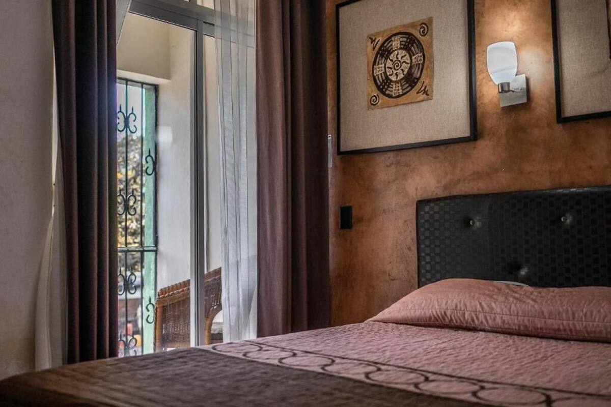 A hotel room with a bed, a wall-mounted light, and a framed artwork.