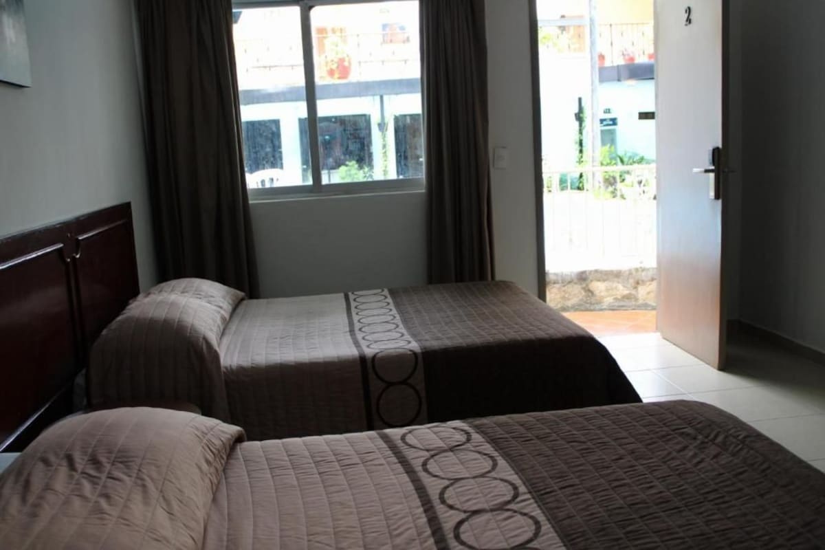 Une chambre avec deux lits, une fenêtre avec des rideaux et une porte donnant sur l’extérieur.
