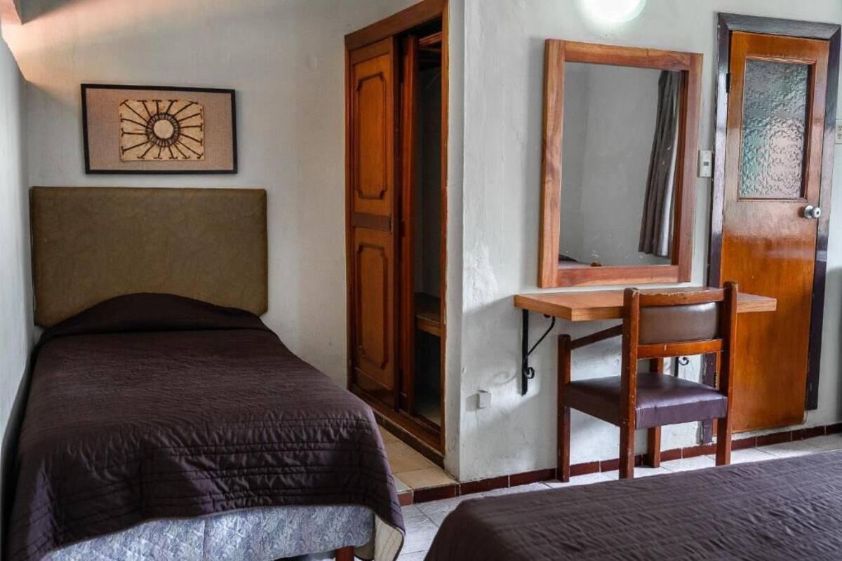 A bedroom with a single bed, a wooden desk, a chair, and a mirror.