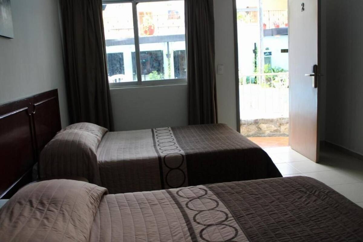 A room with two beds, a window with curtains, and a door leading outside.