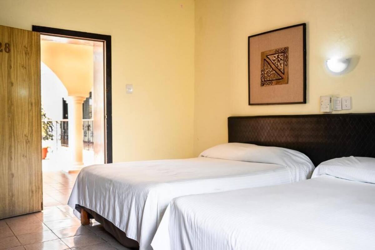 A hotel room with two beds, a wooden door, a framed artwork on the wall, and a light fixture.