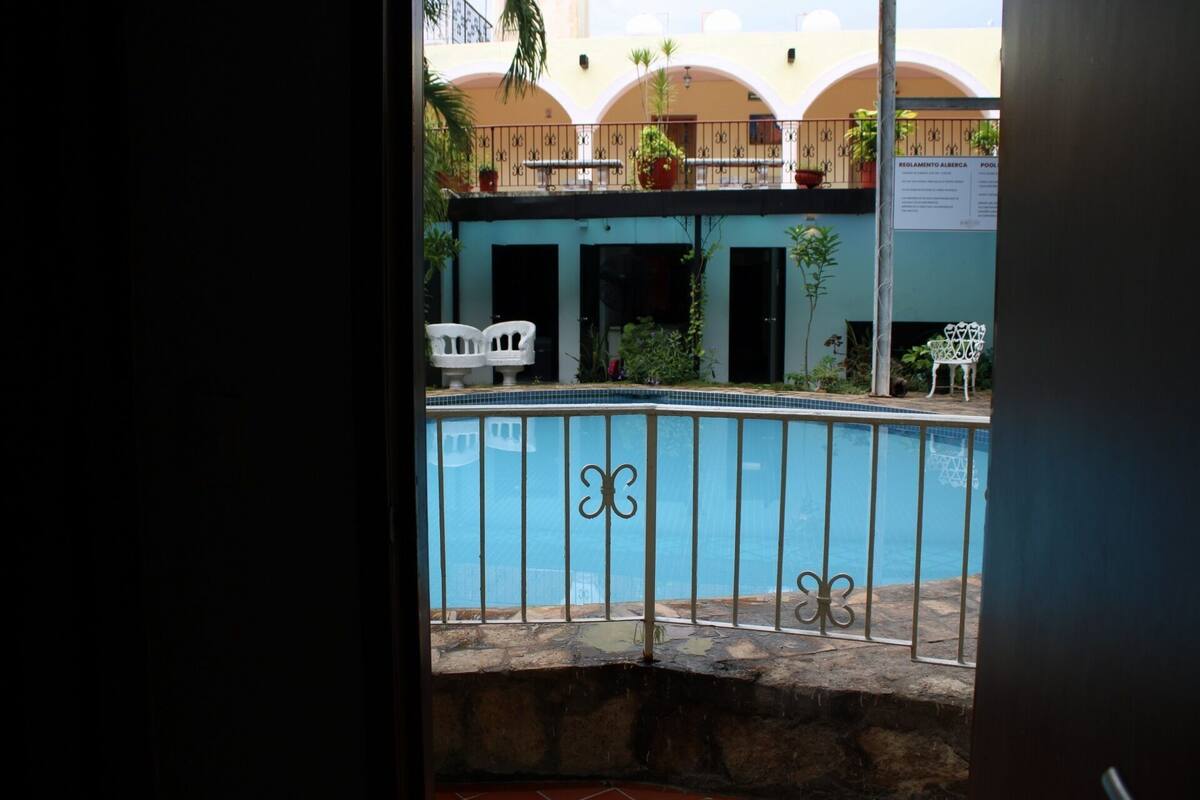 A pool with a metal railing, a building with arches, and outdoor furniture.
