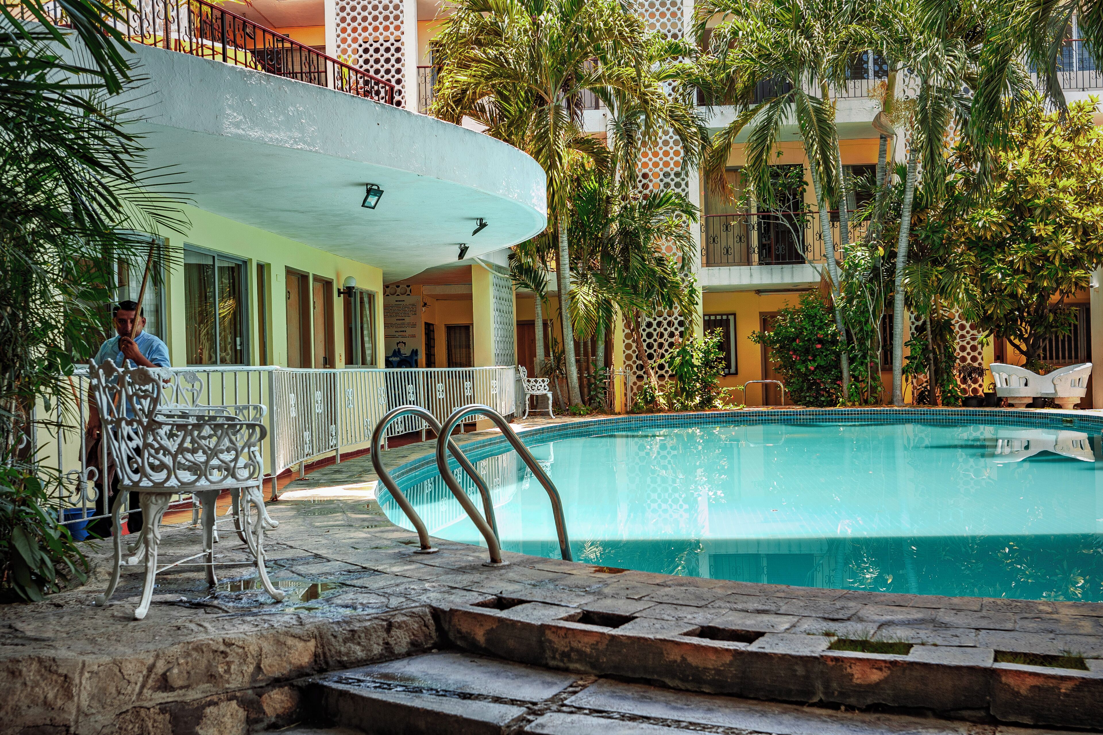 Una piscina con techo curvo, rodeada de palmeras y un edificio con balcones.
