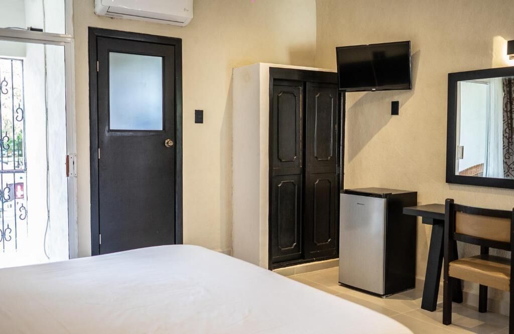 Habitación de hotel con cama, armario, pequeño refrigerador, televisor montado en la pared y una silla.