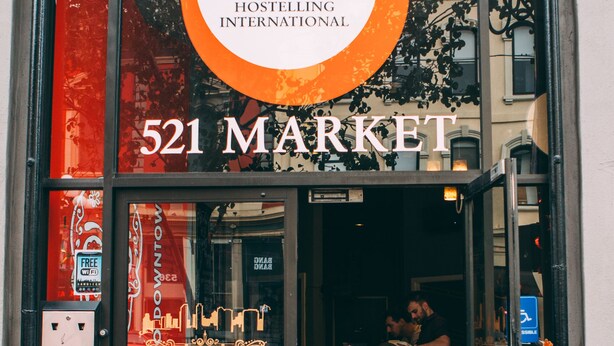 La façade du bureau de Hostelling International situé au 521 Market, avec une vue dégagée sur l’entrée et une personne à l’intérieur.