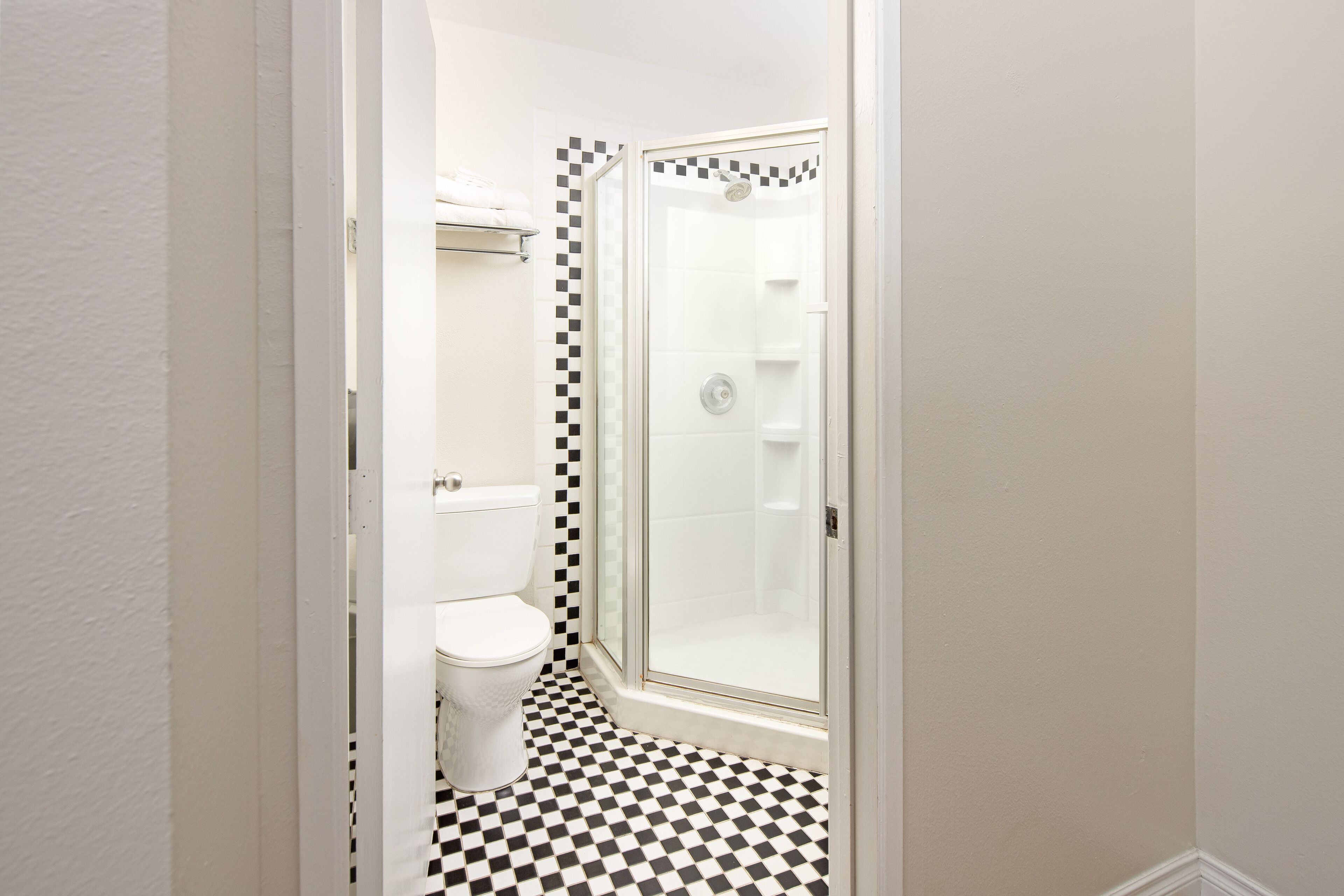 A bathroom with a toilet, a shower with a glass door, and a checkered floor.