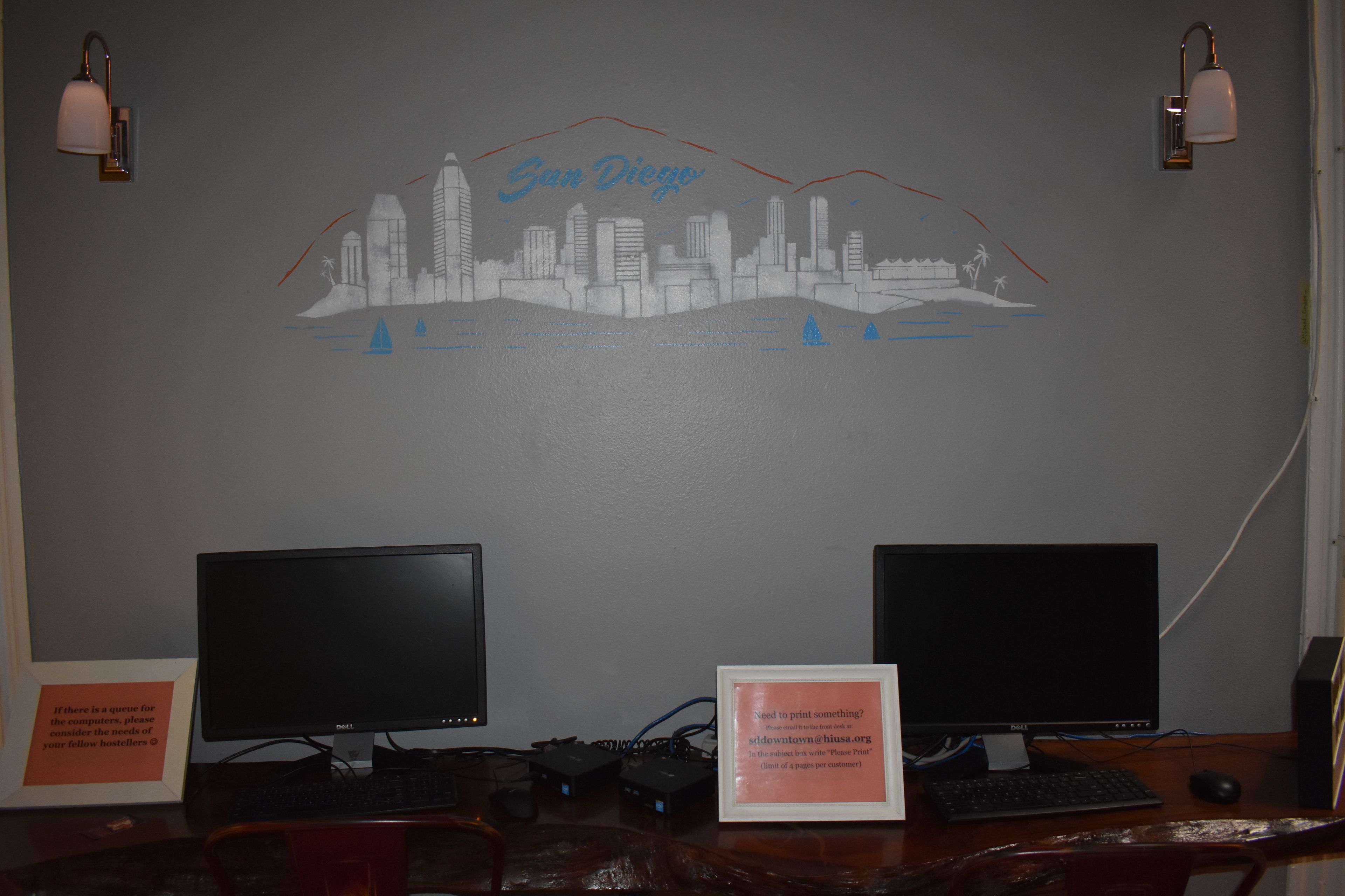 A desk with two monitors, a framed sign, and a wall mural of a city skyline.