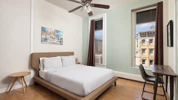 A bedroom with a bed, a ceiling fan, a window with curtains, a small table, and a chair.