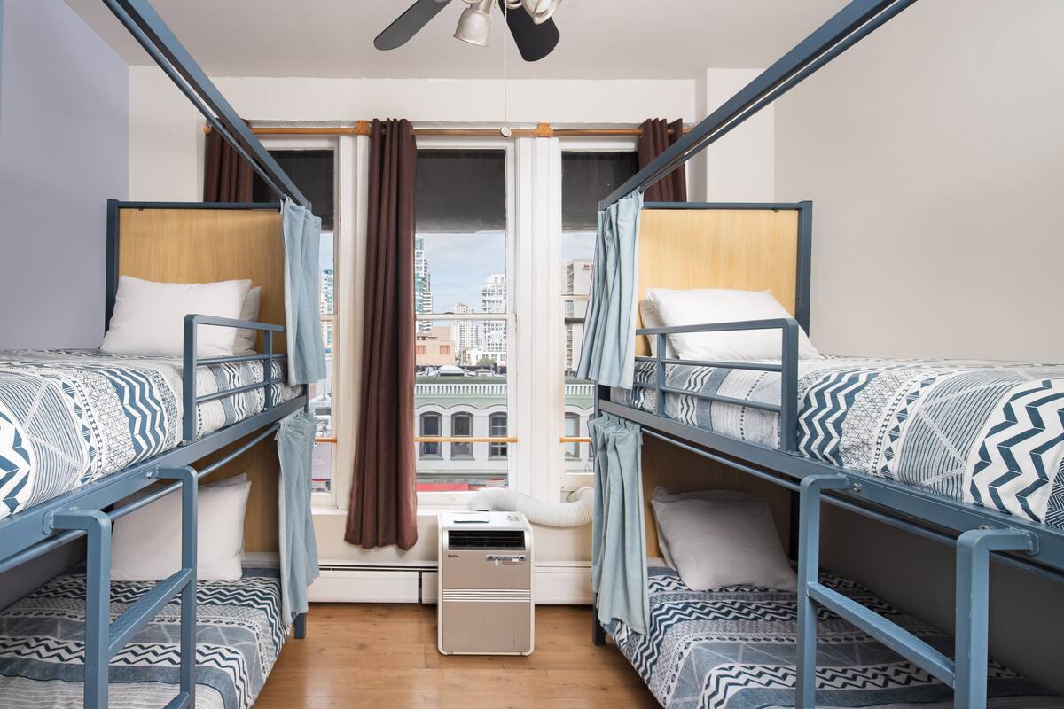 Un dormitorio con dos literas, una ventana con cortinas, un calentador y vistas a edificios.