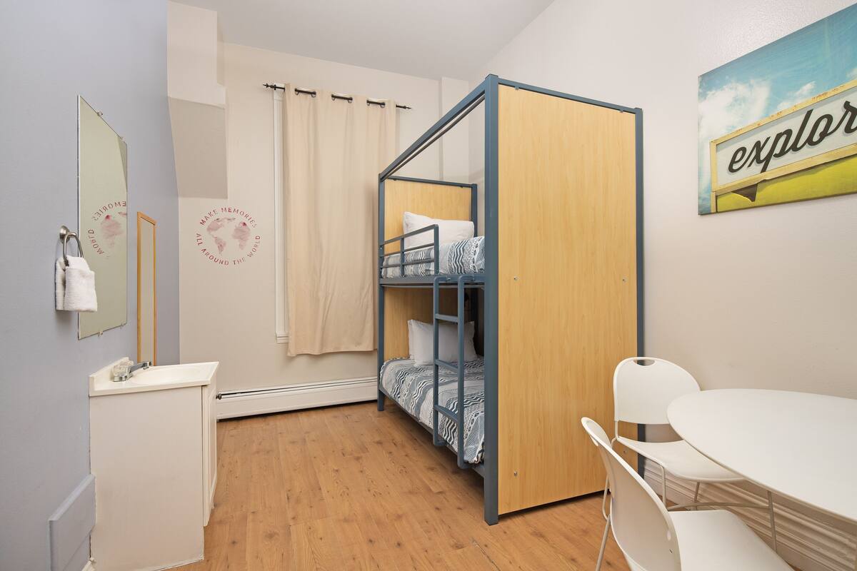 Un dormitorio con literas, un escritorio pequeño con un espejo, una mesa blanca y un cuadro en la pared.